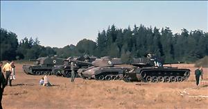 People mill around army tanks parked in a grassy field 